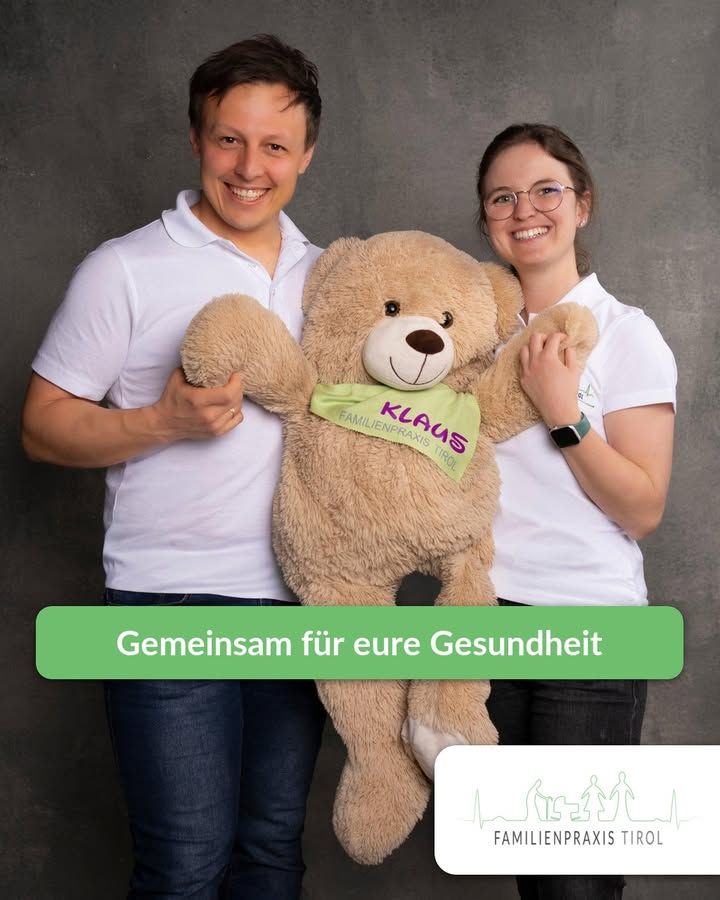 „Gemeinsam für eure Gesundheit“ — Foto zweier Teammitglieder in weißen Praxis-Poloshirts, die zwischen sich einen großen Teddybären halten. Der Bär trägt ein grünes Halstuch mit der Aufschrift „Klaus“ und dem Schriftzug Familienpraxis Tirol.